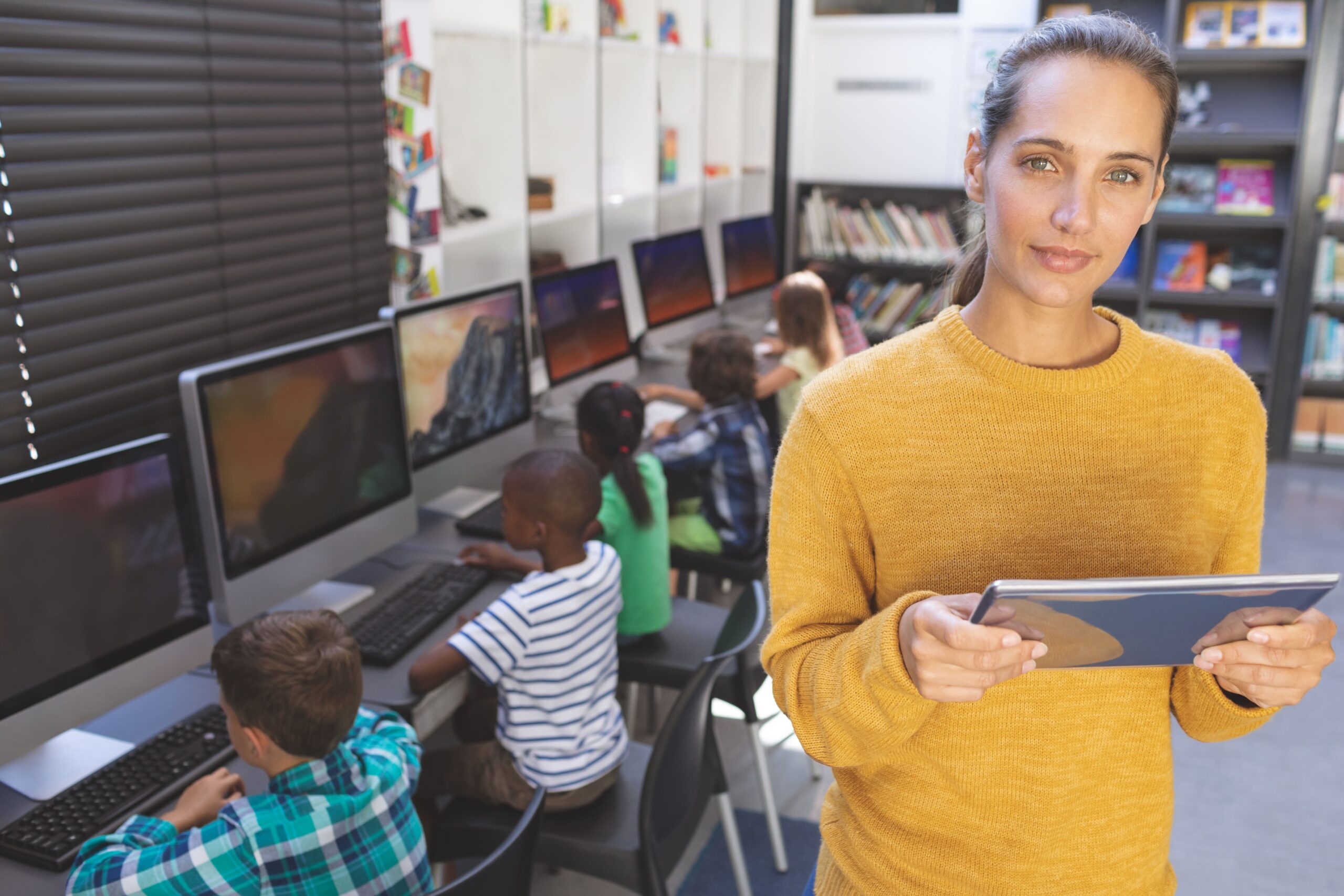 Una profesora con una tablet y sus alumnos trabajando en los ordenadores