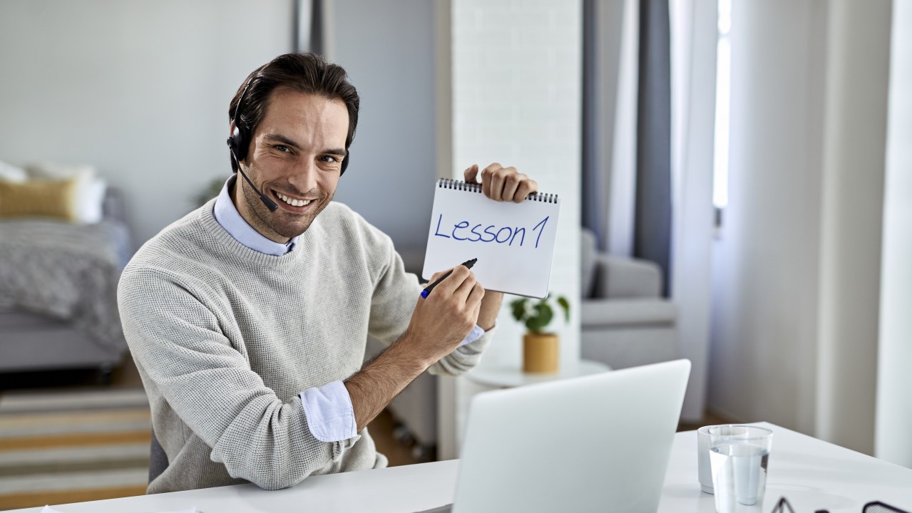 Un profesor dando clases en remoto con "Lesson 1" escrito en un bloc de notas