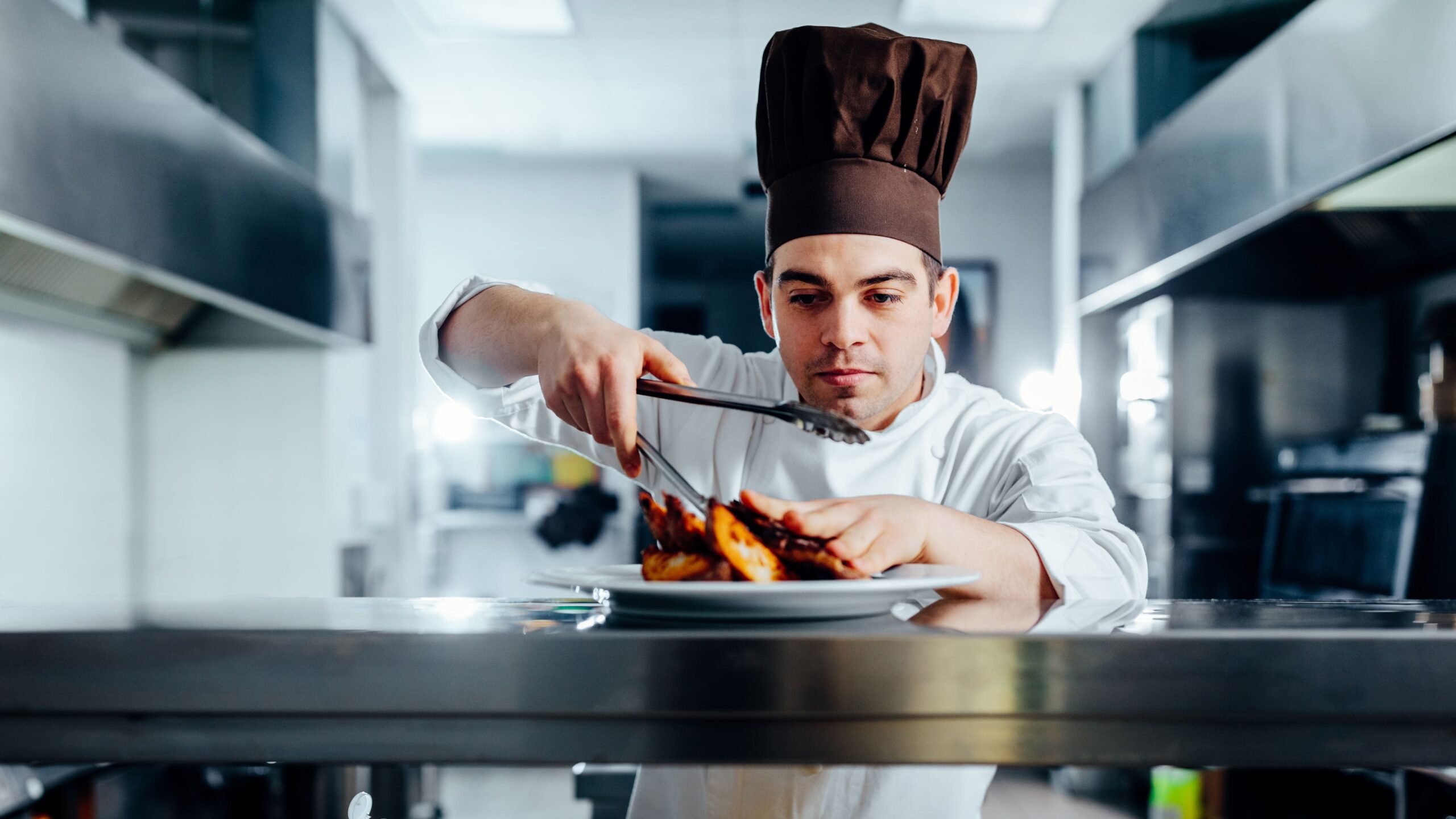 a man in a chef's hat holding tongs to a plate of food