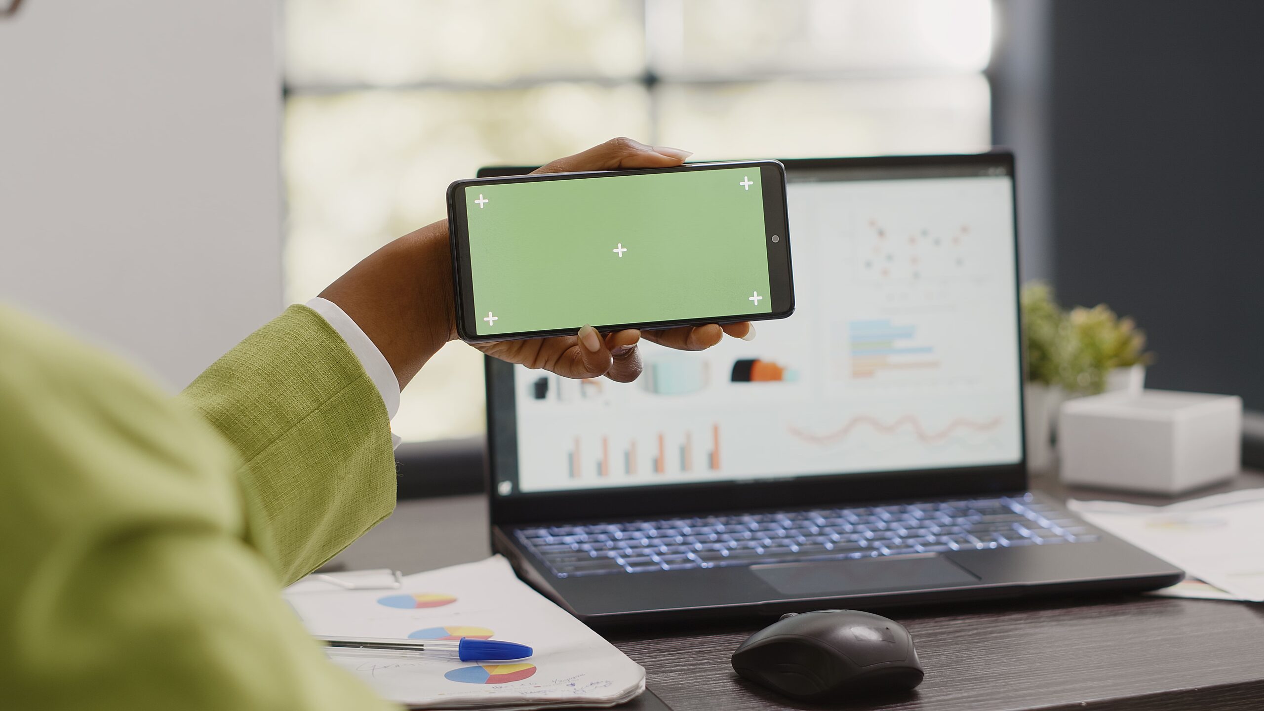 Una persona aguantando su móvil frente a un portátil con diferentes gráficas